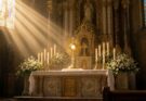 Sunlit Catholic church high altar with the Blessed Sacrament exposed in a gold sunburst monstrance surrounded by candles and white lilies