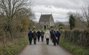 Pilgrims walking a country lane toward a small stone shrine chapel